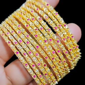 May include: A set of 12 gold bangles with a delicate design featuring small pink and white stones.