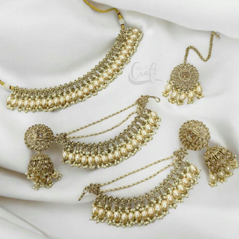 Puede incluir: Un conjunto de collar de oro y perlas que incluye un collar gargantilla, dos collares en capas, un par de pendientes y un maang tikka. El conjunto presenta intrincados dise&ntilde;os de oro y detalles de perlas.