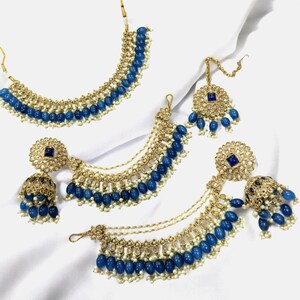 Puede incluir: Un conjunto de joyas de novia indias azul y dorado con un collar, pendientes y un maang tikka. El conjunto presenta cuentas azules, detalles dorados y piedras brillantes.