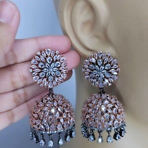 May include: A pair of silver and rose gold earrings with a round, floral design and dangling teardrop-shaped stones.
