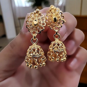 May include: A pair of gold dangle earrings with intricate designs. The earrings feature a bell-shaped pendant with a decorative top.