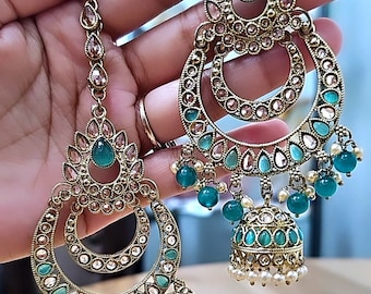 May include: A pair of gold-tone earrings with a turquoise and white design. The earrings feature a large, round hoop with a smaller hoop inside. The hoops are decorated with small, clear stones and turquoise beads. The earrings also have a dangling charm in the shape of a bell.