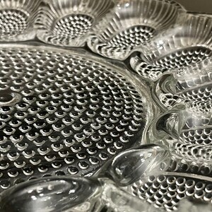 May include: A clear glass serving dish with a textured, raised design. The dish has a central circular section with a repeating pattern of small circles, surrounded by four sections with a more intricate design.