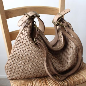 May include: A woven leather handbag with a light brown color. The bag has a long strap and a top handle.