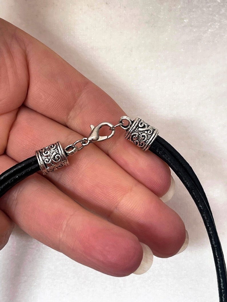May include: A black leather cord necklace with silver-toned clasps and decorative end caps. The cord is flat and has a smooth texture.