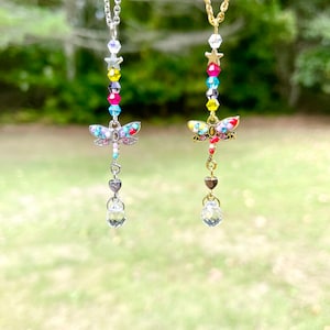 May include: Two delicate necklaces with dragonfly charms. One necklace has a silver chain with a clear crystal pendant and a rainbow of beads. The other necklace has a gold chain with a clear crystal pendant and a rainbow of beads.