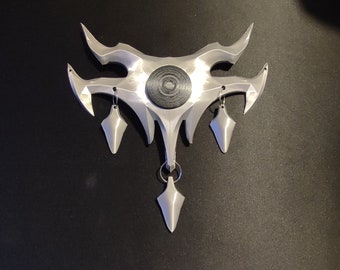 May include: A silver-coloured, 3D printed, geometric pendant with a circular, black and silver design in the centre. The pendant has three dangling, pointed, silver-coloured ornaments.
