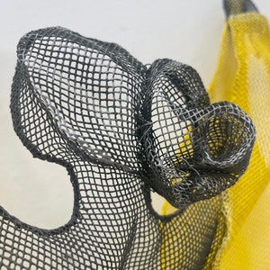 May include: A close-up of a black mesh sculpture with a yellow mesh sculpture in the background. The black mesh is formed into a shape that resembles a flower.