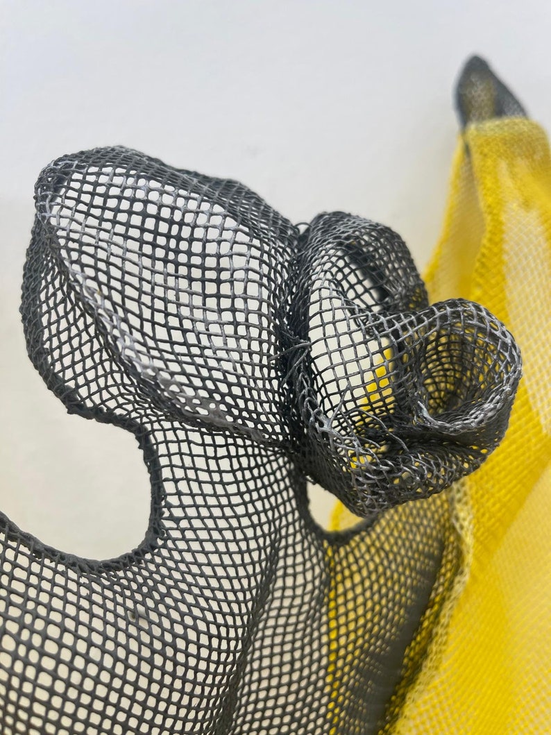 May include: A close-up of a black mesh sculpture with a yellow mesh sculpture in the background. The black mesh is formed into a shape that resembles a flower.