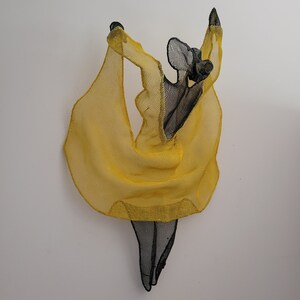May include: A wire sculpture of a person in a yellow dress, with the person's arms raised above their head.