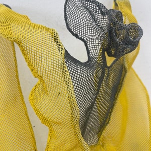 May include: A black and yellow mesh sculpture with a flowing, abstract form. The sculpture is made of wire mesh and is painted in a bright yellow and black color scheme.