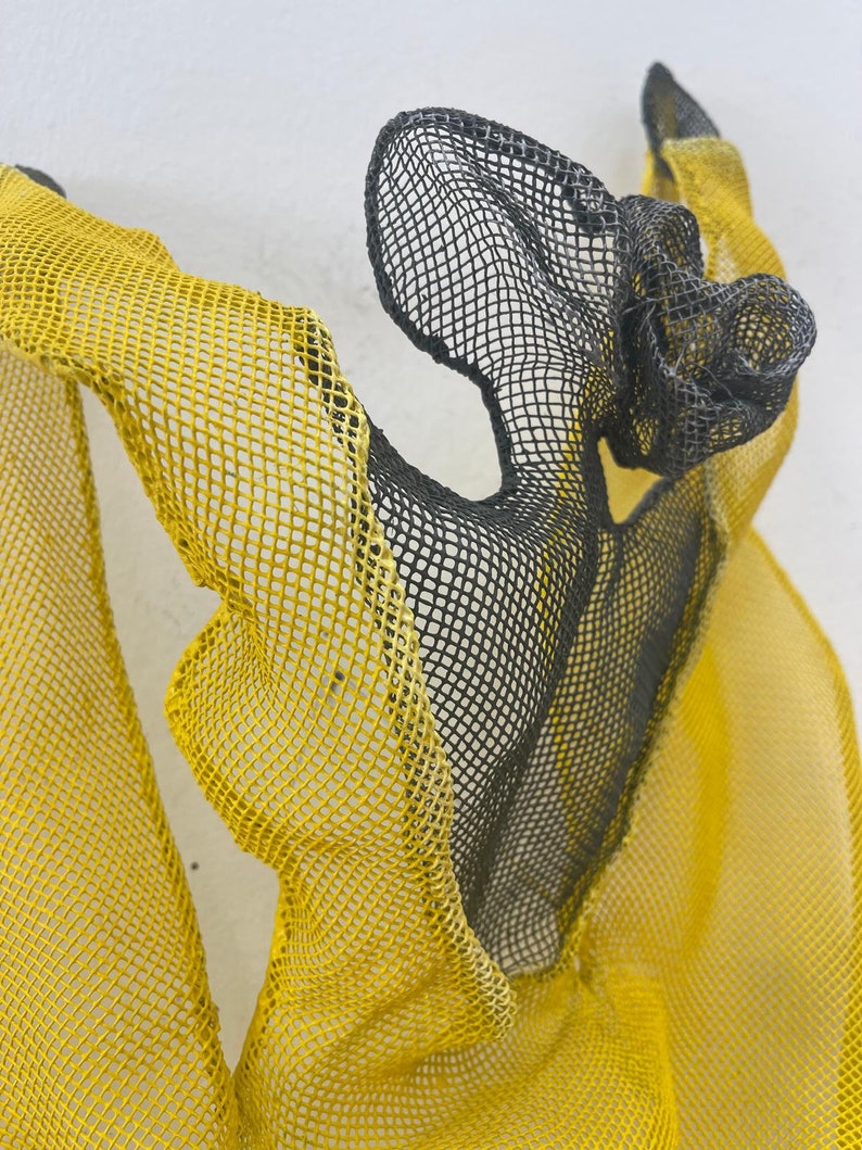 May include: A black and yellow mesh sculpture with a flowing, abstract form. The sculpture is made of wire mesh and is painted in a bright yellow and black color scheme.