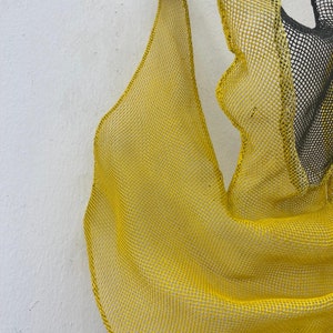 May include: A yellow mesh sculpture with a flowing, organic shape. The mesh is made of a fine, woven material and has a slightly textured surface.