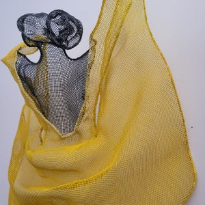 May include: A yellow and black mesh sculpture with a flowing, draped design. The sculpture is made of woven wire and has a delicate, airy appearance.