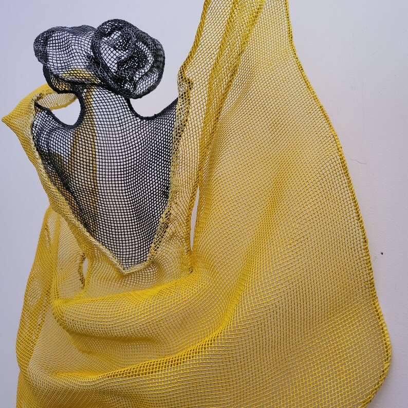 May include: A yellow and black mesh sculpture with a flowing, draped design. The sculpture is made of woven wire and has a delicate, airy appearance.