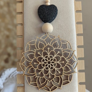 Könnte beinhalten: Ein Holz-Mandala-Anhänger mit einem schwarzen Lavastein-Herz, das an einer Schnur aus Holzperlen hängt.