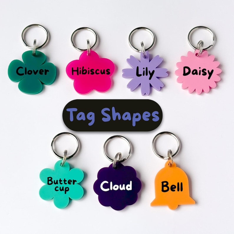 May include: A collection of colorful pet tag shapes, including clover, hibiscus, lily, daisy, buttercup, cloud, and bell designs. Each tag has a silver keyring. The text "Tag Shapes" is displayed on a black oval.