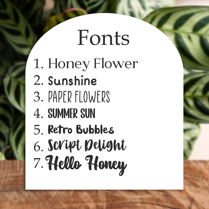 May include: A white card with the word "Fonts" at the top, listing seven font names: Honey Flower, Sunshine, PAPER FLOWERS, SUMMER SUN, Retro Bubbles, Script Delight, and Hello Honey. The card is set against a background of green leaves and a wooden surface.