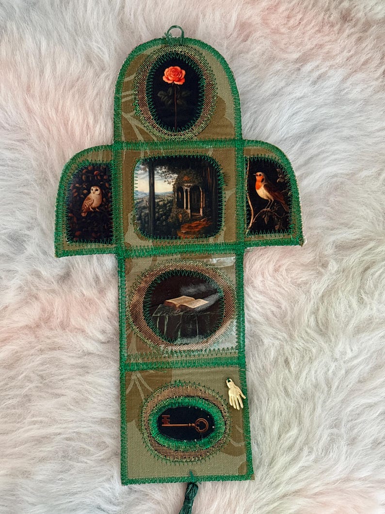 K&ouml;nnte beinhalten: Ein handgefertigtes Stoffkunstwerk mit einem gr&uuml;nen und goldenen Blumenmuster. Es zeigt ovale Tafeln mit Bildern einer Rose, einer Eule, einer Landschaft, eines Rotkehlchens, eines offenen Buches, eines Schl&uuml;ssels und einer kleinen goldenen Hand. Die R&auml;nder sind mit gr&uuml;nem Faden gen&auml;ht.