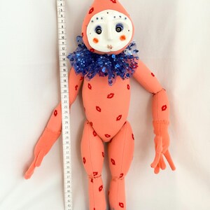 Puede incluir: Mu&ntilde;eca hecha a mano con cuerpo color melocot&oacute;n y cabeza en forma de cono. La mu&ntilde;eca tiene una cara de m&aacute;scara blanca, un cuello de lentejuelas azules y detalles rojos en forma de labios. La mu&ntilde;eca mide unos 122 cm de altura.
