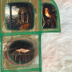 K&ouml;nnte beinhalten: Ein handgefertigtes Textilkunstwerk mit Patchwork-Design. Es zeigt kleine, gerahmte Bilder eines Vogels, eines Pavillons und eines offenen Buches. Das St&uuml;ck ist mit gr&uuml;nen N&auml;hten und goldenen Akzenten versehen, vor einem strukturierten Hintergrund.