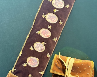 May include: A long, dark brown velvet strip featuring six oval-shaped animal portraits and small embroidered leaf accents, paired with a matching folded velvet pouch secured with a light yellow ribbon tie. Both items have frayed edges.