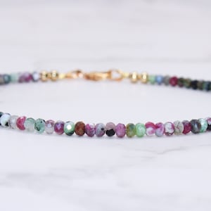 Puede incluir: Un delicado brazalete de piedras preciosas multicolores con un cierre de oro. El brazalete presenta una variedad de piedras preciosas verdes, rosas y marrones.