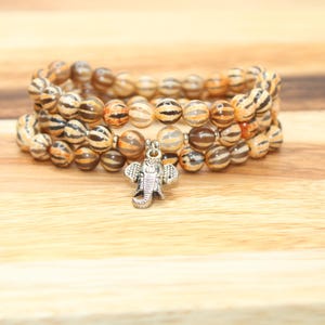 May include: A triple-strand bracelet made of brown and white striped beads with a silver elephant charm.