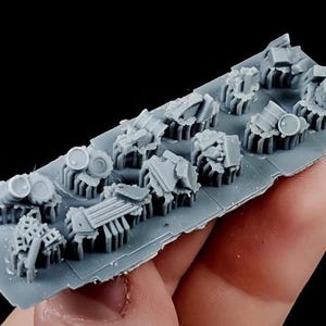 May include: A gray plastic sprue with miniature, detailed, architectural ruins. The sprue contains various pieces, including what appear to be barrels, broken columns, and rubble. The pieces are designed for model building or tabletop gaming.