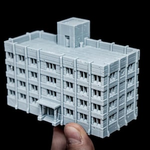 Puede incluir: Maqueta de edificio gris claro con múltiples pisos y ventanas. El modelo tiene un techo plano con una pequeña estructura encima. El edificio se sostiene sobre un fondo negro.