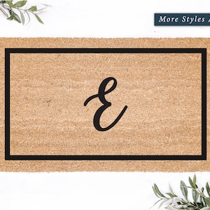 May include: A brown coir doormat with a black border and the letter "E" in a cursive font.