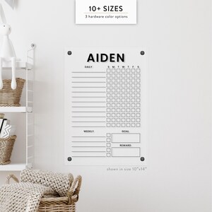 May include: A clear acrylic chore chart with the name "AIDEN" at the top. The chart includes sections for daily and weekly tasks, goals, and rewards. The text "10+ SIZES" and "3 hardware color options" are at the top. The size shown is 10"x14".