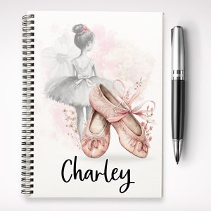 May include: A pink spiral notebook featuring a watercolour illustration of ballet shoes and a ballerina. The notebook is personalised with the name "Charley" on the front.