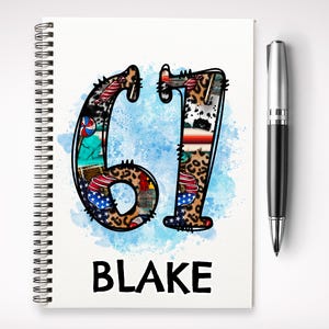 May include: A spiral-bound notebook displaying the number "61" in a collage style, incorporating leopard print, American flags, and other designs. The name "BLAKE" is printed in bold, black letters beneath the number. A silver and black pen is positioned to the right.