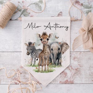 May include: A white canvas banner with the names "Milo Anthony" printed in black cursive script. The banner features a watercolour illustration of a giraffe, zebra, and elephant with green foliage and butterflies.