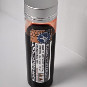 May include: A black glass vial with a silver lid containing a red liquid. The label reads "GLOBAL RELIEF EFFORT" and includes information about a volatile end stage infection, a blood sample, and a quarantine zone.