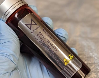 Puede incluir: Un vial de vidrio con tapa plateada y una etiqueta que dice "MONARCH Kaiju-[Godzilla] Sample-[Blood] Location-[Tokyo/Japan]". El vial contiene un líquido rojo oscuro y un símbolo de peligro biológico.