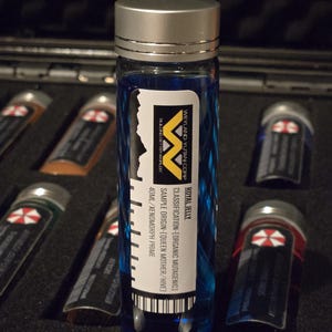 May include: A blue glass vial with a silver cap and a white label. The label reads "ROYAL JELLY", "WEYLAND-YUTANI CORP", "CLASSIFICATION-[ORGANIC MUTAGENIC]", "SAMPLE ORIGIN-[QUEEN MOTHER/HIVE]", "40ML/XENOMORPH PRIME".