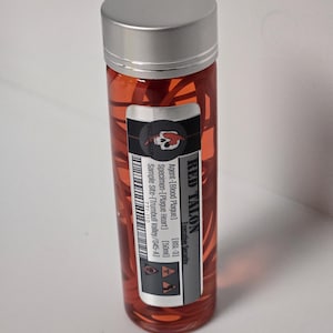 May include: A small, clear glass bottle with a silver lid filled with a red liquid and red pepper flakes. The bottle has a black and white label with the text "RED TALON", "Agent-[Blood Plague]" and "Specimen-[Plague Heart] [50ml]" printed on it.
