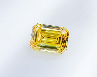 May include: A vivid, emerald-cut yellow diamond. The gemstone's facets catch the light, highlighting its colour and clarity. The rectangular shape and bright hue make it a striking piece.