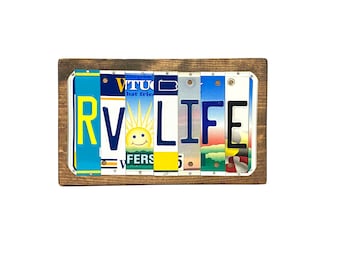 May include: A wooden sign with the word "RV LIFE" spelled out using vintage license plates. The letters are in various colors and have different designs, including a smiley face and a sun.