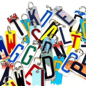 May include: A collection of colorful license plate letter charms with silver key rings. The letters are in various colors, including red, blue, yellow, green, and white. The letters are all uppercase and are attached to the key rings with a small metal loop.