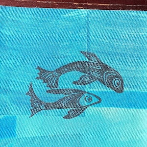 Peut inclure: Deux silhouettes de poissons noirs imprimées sur un fond de tissu bleu clair.