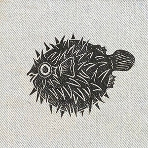 May include: Black and white illustration of a pufferfish with spiky fins on a white fabric background.