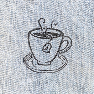 May include: A black and white illustration of a teacup with a tea bag and steam rising from the top, printed on a blue denim fabric.