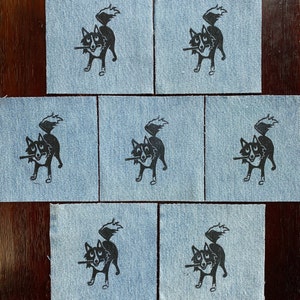 Op de afbeelding: Set van tien blauwe denim patches met zwarte inkt illustraties van een hond met een stok in zijn bek. De hond kijkt naar links en heeft zijn staart over zijn rug gekruld.