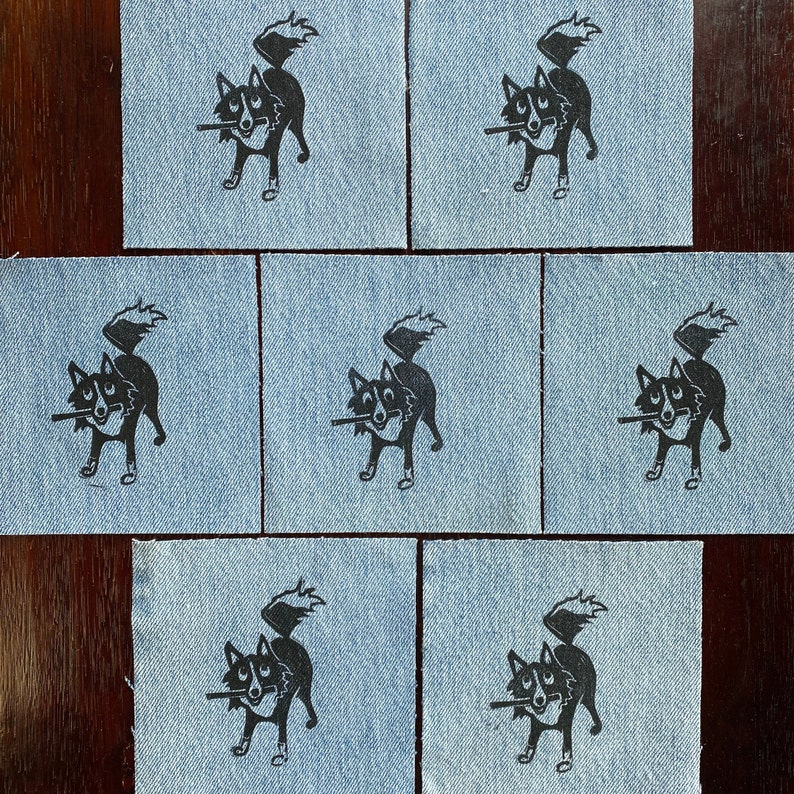 Op de afbeelding: Set van tien blauwe denim patches met zwarte inkt illustraties van een hond met een stok in zijn bek. De hond kijkt naar links en heeft zijn staart over zijn rug gekruld.