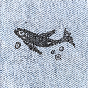 Op de afbeelding: Een zwart silhouet van een vis die zwemt op een blauwe denim achtergrond met kleine witte cirkels eromheen.