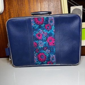Könnte beinhalten: Ein vintage marineblauer Koffer mit einem floralen Mittelteil. Das Mittelteil weist ein lebendiges Muster aus rosa, blauen und lila Blumen auf. Der Koffer hat eine silberne Zierleiste und einen silbernen Griff.