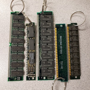 May include: Four green circuit boards with gold connectors and text on them are attached to key rings. The circuit boards are labeled with the text "NANYA NT511740CSJ-60", "SIEMENS HYB5110008J-70 9147", "MSC2304-15YS9A 71116", and "KM44C4100AJ-7".